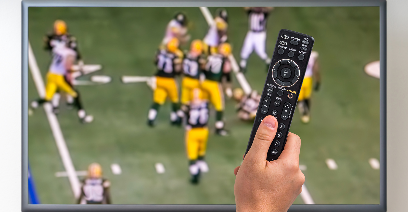 Man holding TV remote with football on in the background