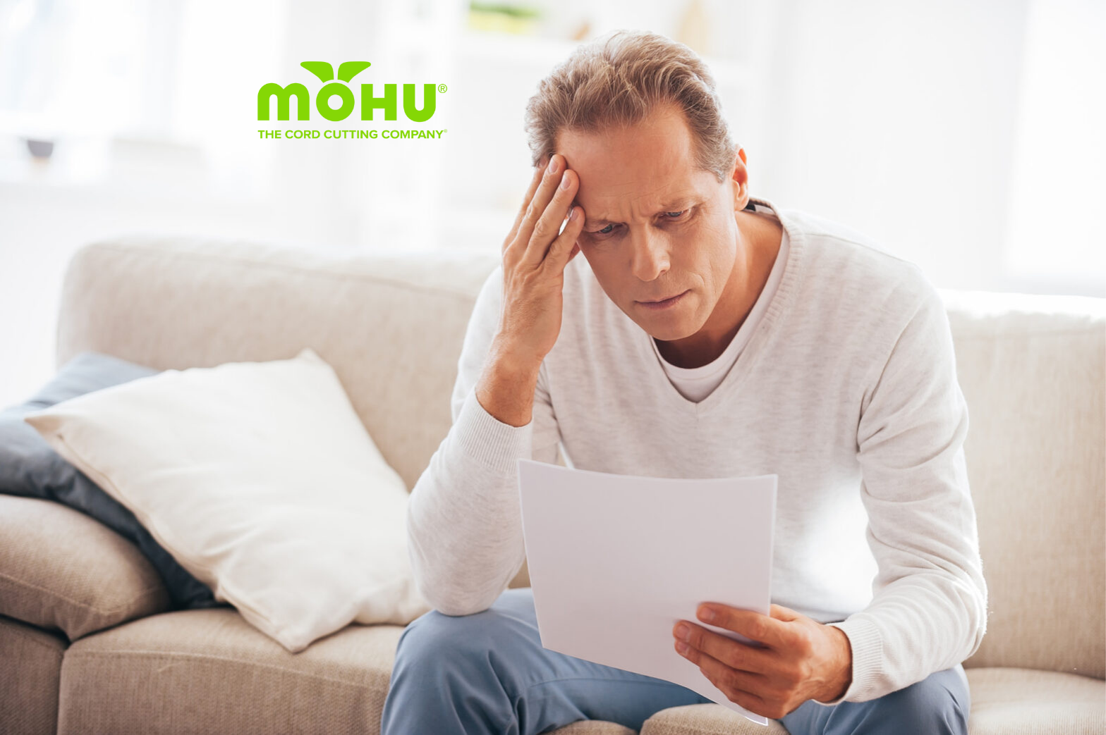 Man looking at bill sitting on couch with hand on his head and Mohu logo on top
