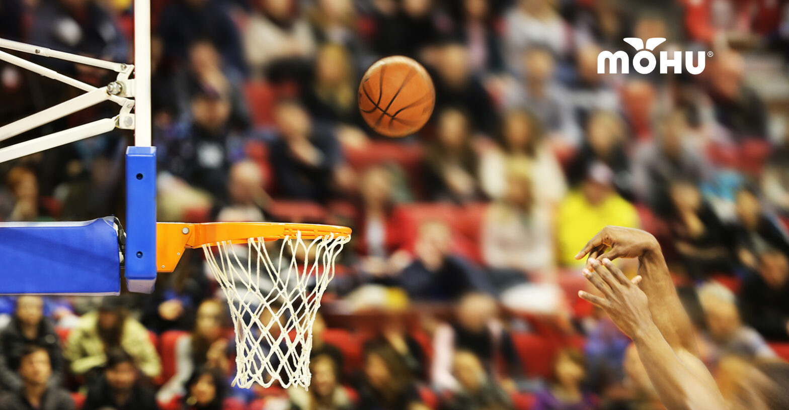 Basketball going into hoop with crowd watching in the background and Mohu logo