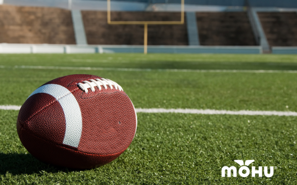 football resting on football field with stadium in background and mohu logo