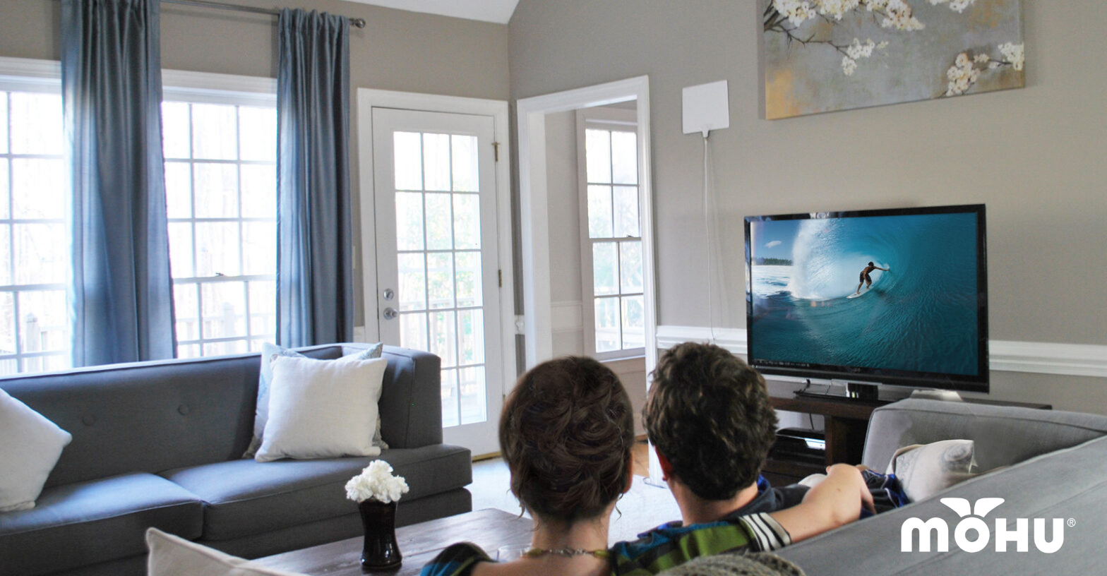 man and woman sitting on the couch watching tv mohu logo